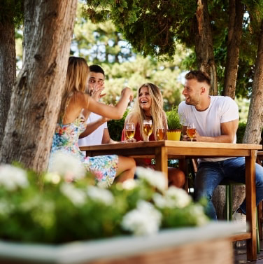 Friends laughing while sitting at outdoor table with drinks